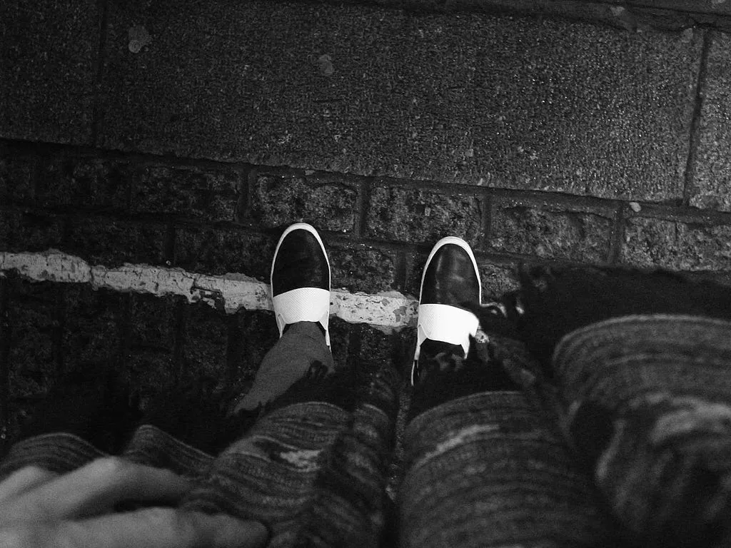 Black-and-white photo of a person sitting on a curb, looking down at their shoes