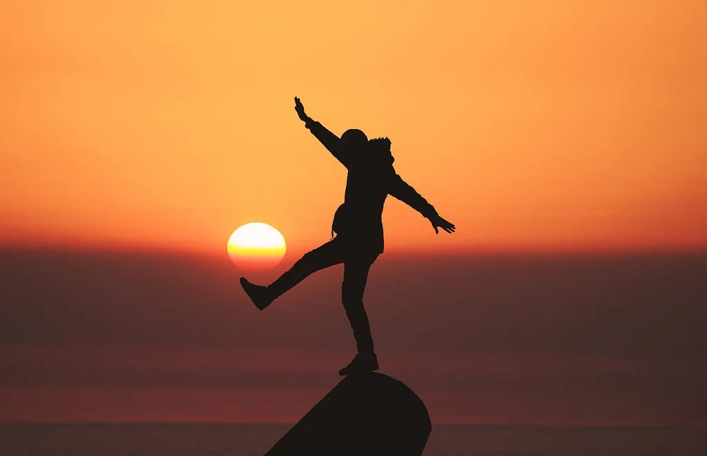 Silhouette of a person balancing on one leg on a rock against an orange sunset