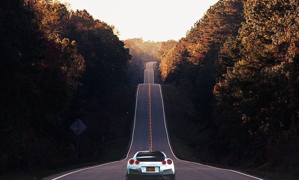 A car driving on a long, straight road through autumn woods